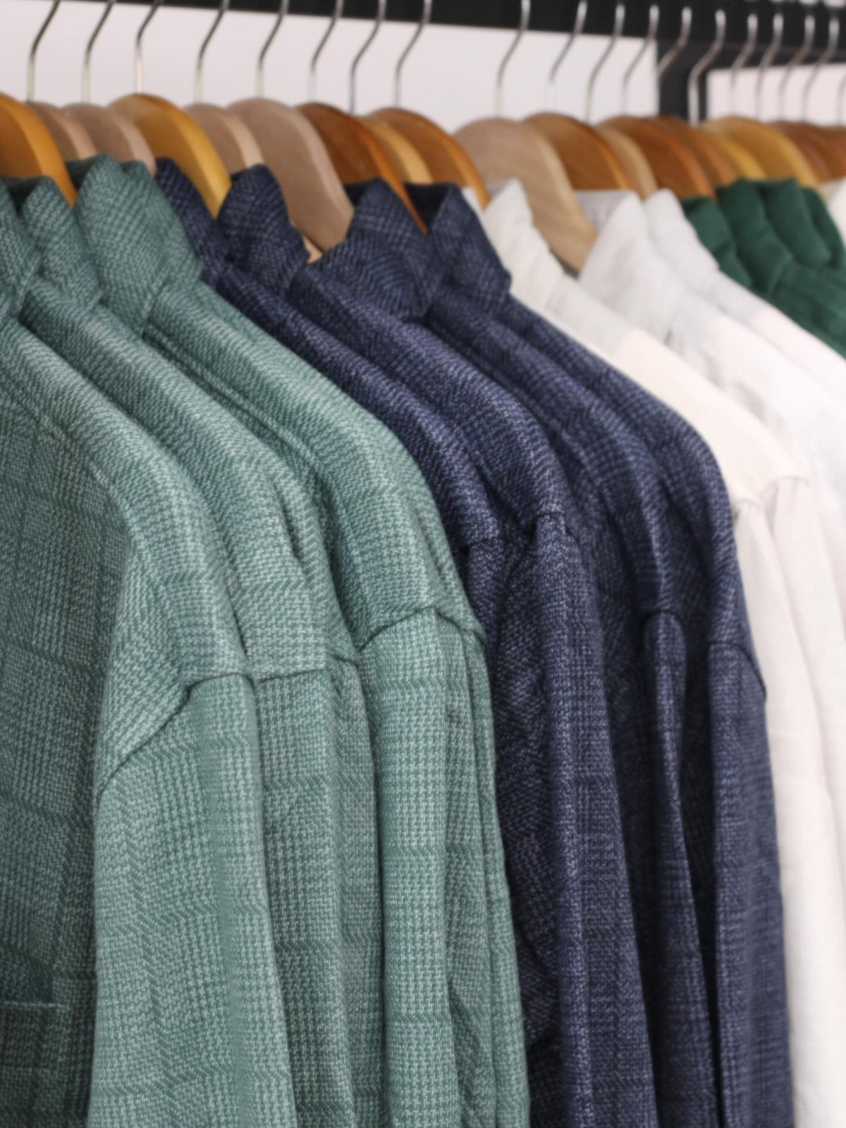 Green, navy and white shirts on wooden hangers