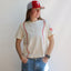 Woman wearing cream baseball stitch tee with red Phillies P logo and red/white baseball stitching design, paired with jeans …