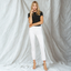 Woman wearing black short-sleeve tee with white mid-rise ankle straight jeans and tan strappy sandals against white draped b…