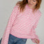 Woman wearing pink and cream striped henley with white button placket and long sleeves, paired with blue jeans
