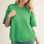 Woman wearing a green sweater and blue jeans on a plain background