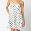 Woman wearing a white dress with black polka dots against a plain background