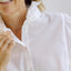 Woman wearing a white blouse with ruffled collar against a plain background