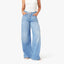 Woman wearing white tank top and light blue wide-leg drawstring jeans with white sneakers, hands in pockets