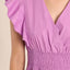 Close-up of a person wearing a purple dress with ruffled sleeves on a beige background