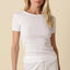 Woman wearing a white ribbed top and pants against a beige background