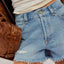 Person wearing denim shorts with a brown leather jacket on a neutral background