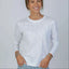 Woman wearing white long sleeve shirt with jeans and bracelets against gray background. 