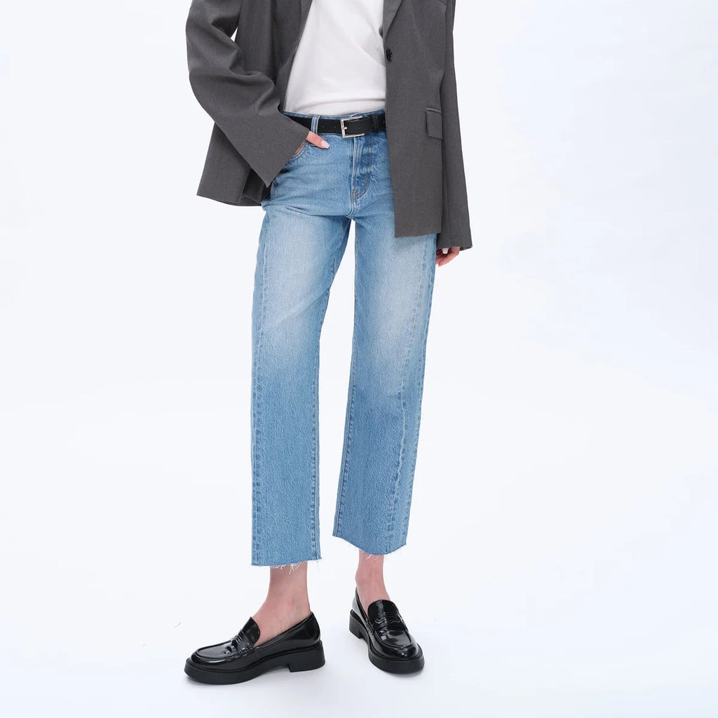 Woman wearing high rise straight leg cropped jeans in light blue denim with black loafers, white top, and charcoal blazer