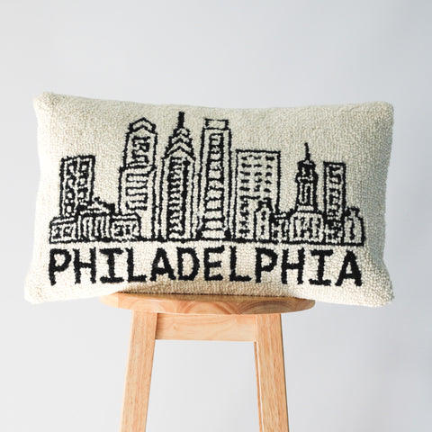 Cream colored hook pillow with black Philadelphia skyline and 'PHILADELPHIA' text displayed on wooden stool