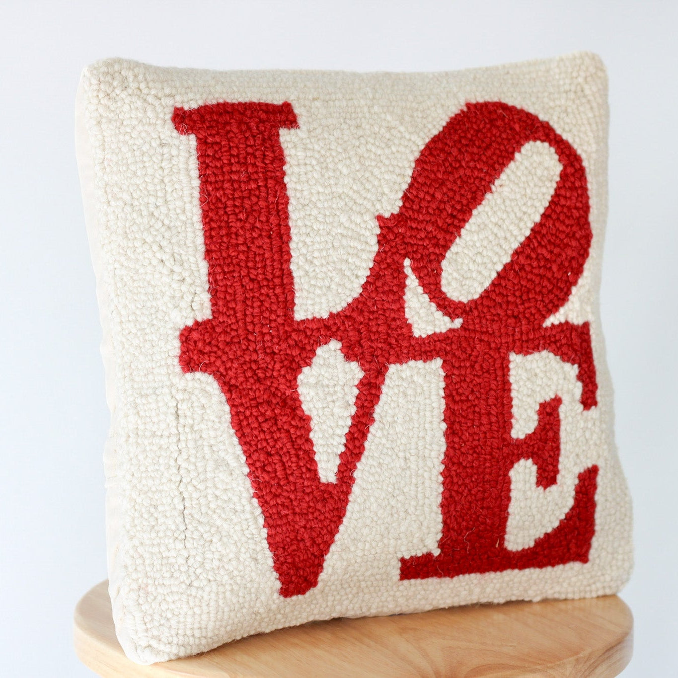Cream wool hooked pillow with red LOVE typography design, featuring stylized letters on a textured white background