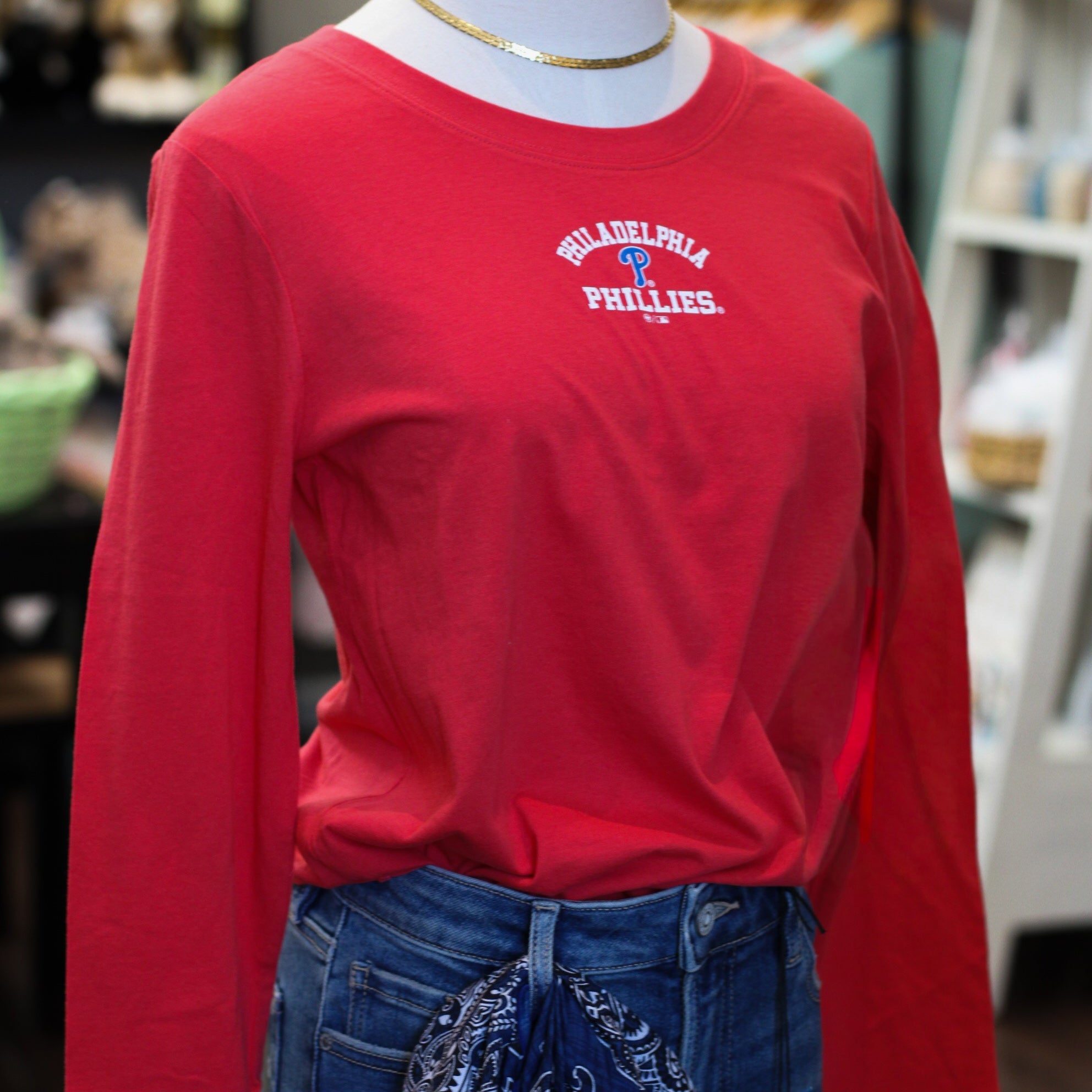 Red long-sleeve Philadelphia Phillies tee with white arch logo and blue P symbol, styled with dark jeans and gold chain neck…
