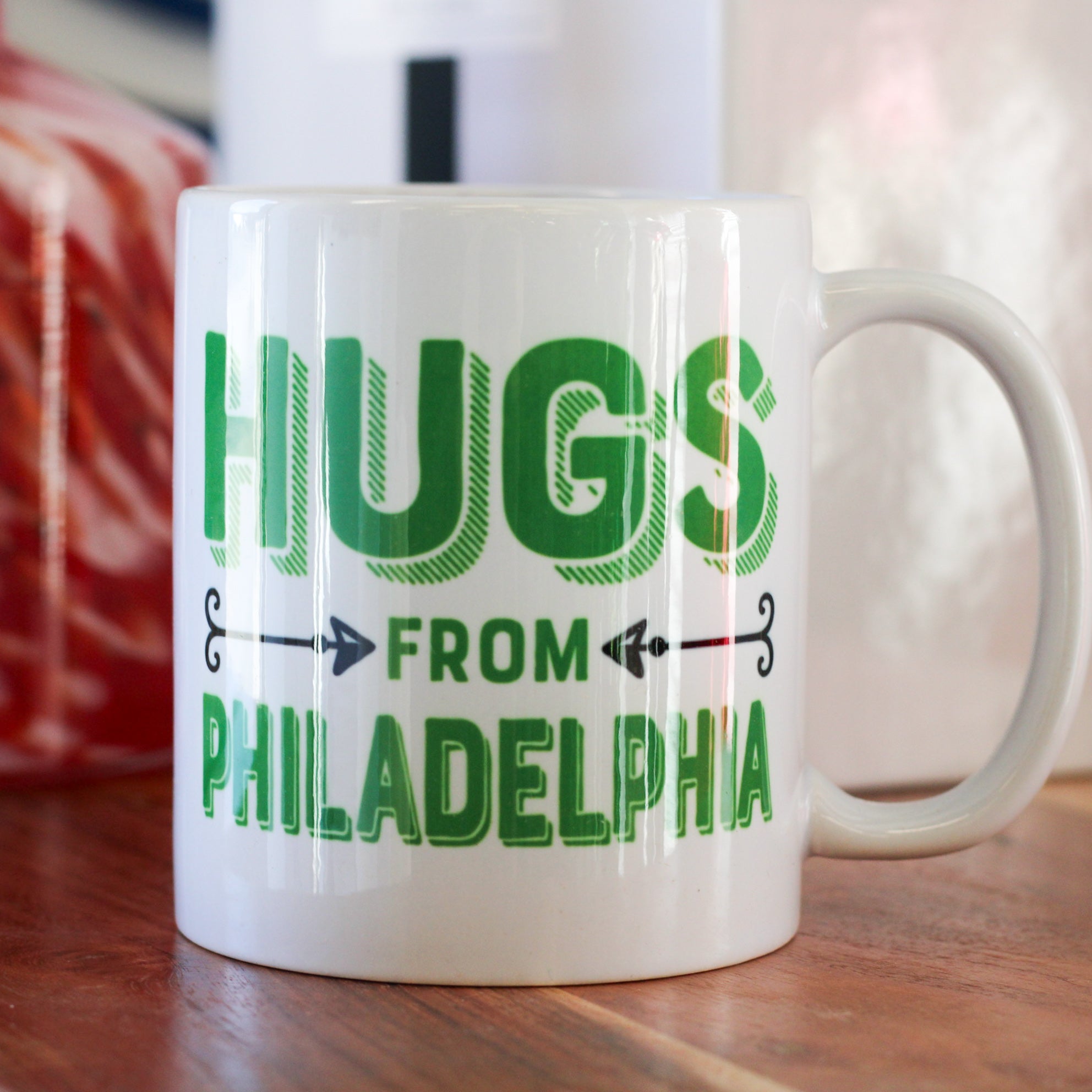 White ceramic mug with green text reading 'Hugs From Philadelphia' with directional arrows, Philadelphia sports fan gift