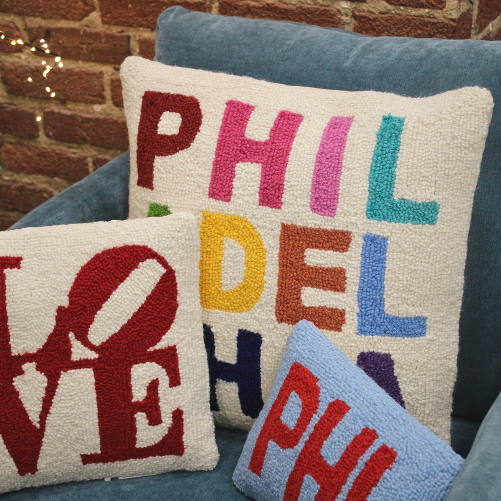 Three colorful hooked pillows with Philadelphia-themed text including 'PHIL', 'LOVE', and 'DEL' in multicolored letters on c…