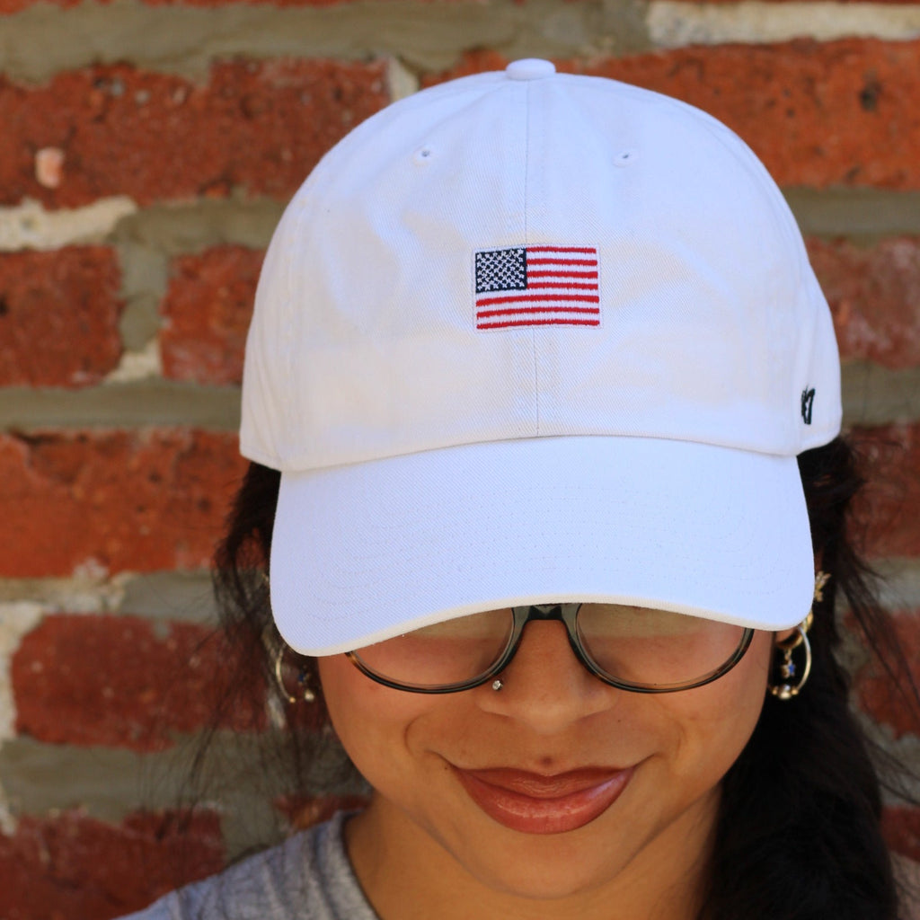 Person wearing a white cap with an American flag design against a brick wall.
