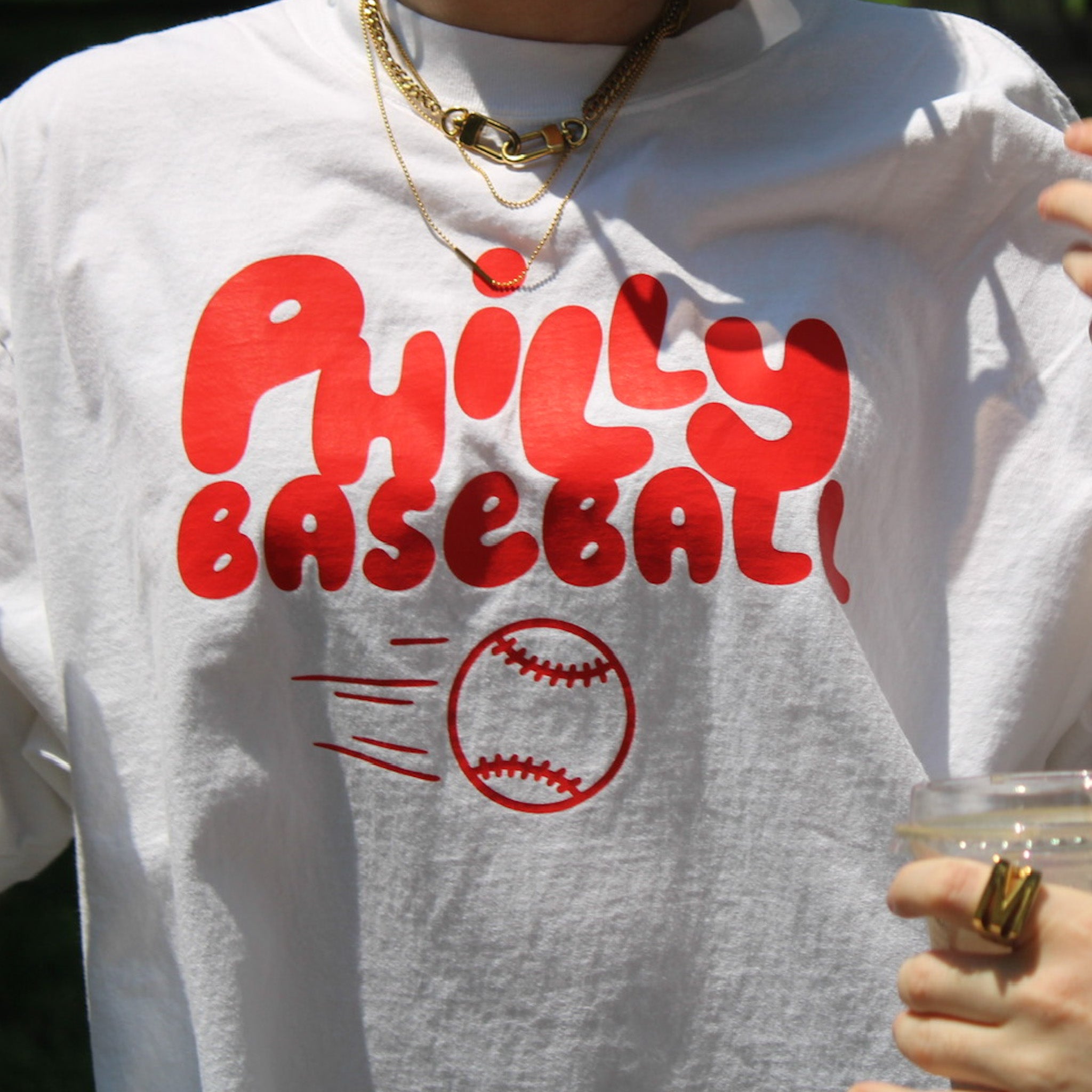 White sweatshirt with red 'Philly Baseball' text and a baseball graphic, held by a person.