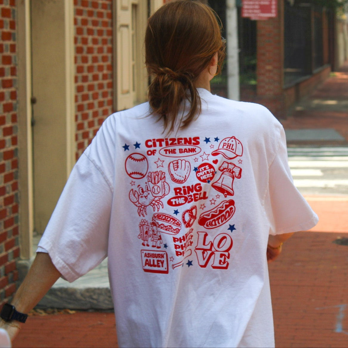 Woman wearing white drop shoulder tee with red Philadelphia Phillies baseball collage design featuring sports icons and 'PHL… Main image