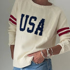 Cream knit sweater with navy USA lettering and burgundy striped sleeves, styled with denim and silver bracelets