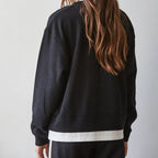 Person wearing a black sweatshirt with a white connected t shirt on a plain background