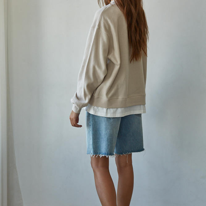 Woman wearing a beige sweater and denim shorts against a plain background