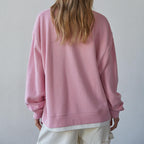 Person wearing a pink sweatshirt and light-colored shorts against a plain background