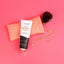 Anti-Granny Hands Orange Vanilla hand cream tube displayed with peach quilted wallet, sunglasses, and gold jewelry on pink b…