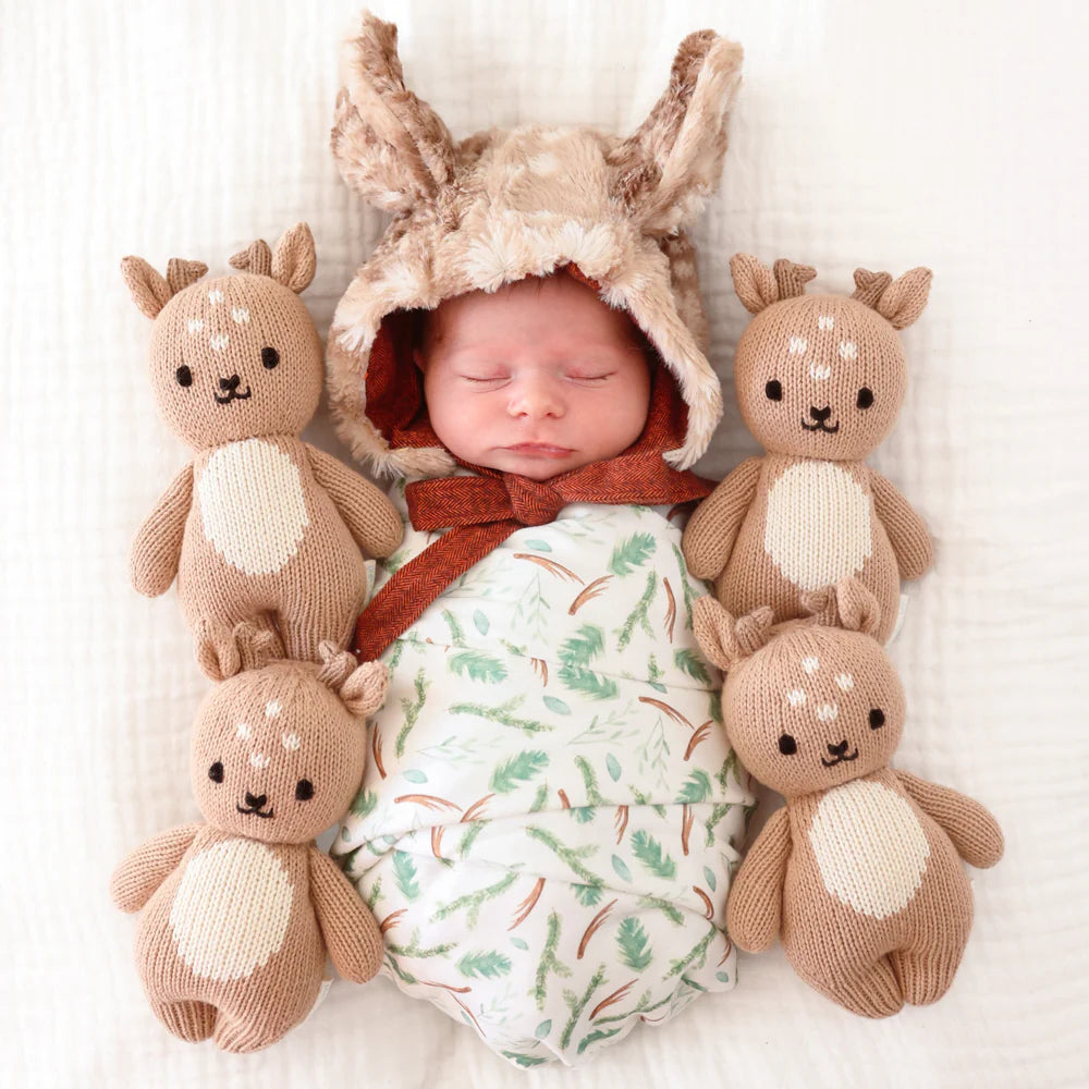 Newborn baby wearing a bunny hat surrounded by knit deer toys on a white background