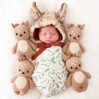 Newborn baby wearing a bunny hat surrounded by knit deer toys on a white background