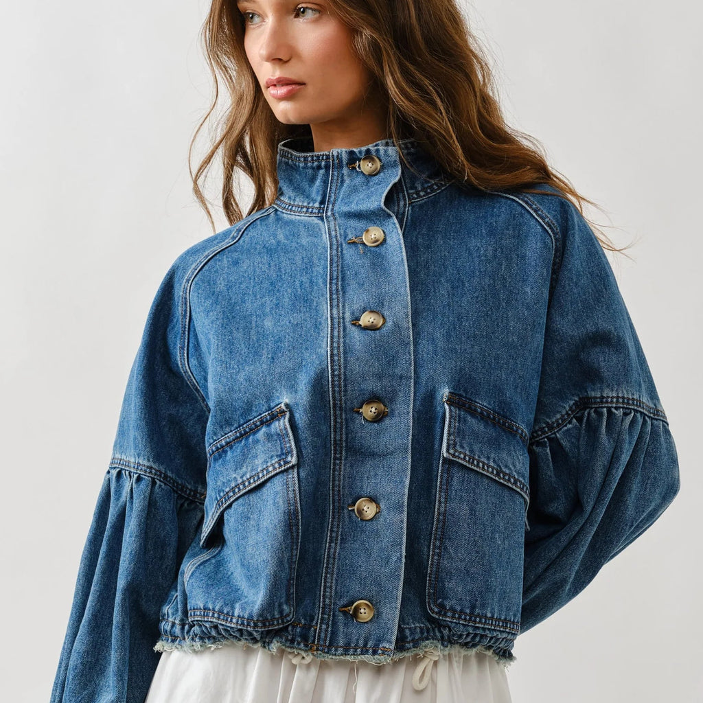 Woman wearing medium-wash denim jacket with balloon sleeves, front button closure, chest pockets, and frayed hem