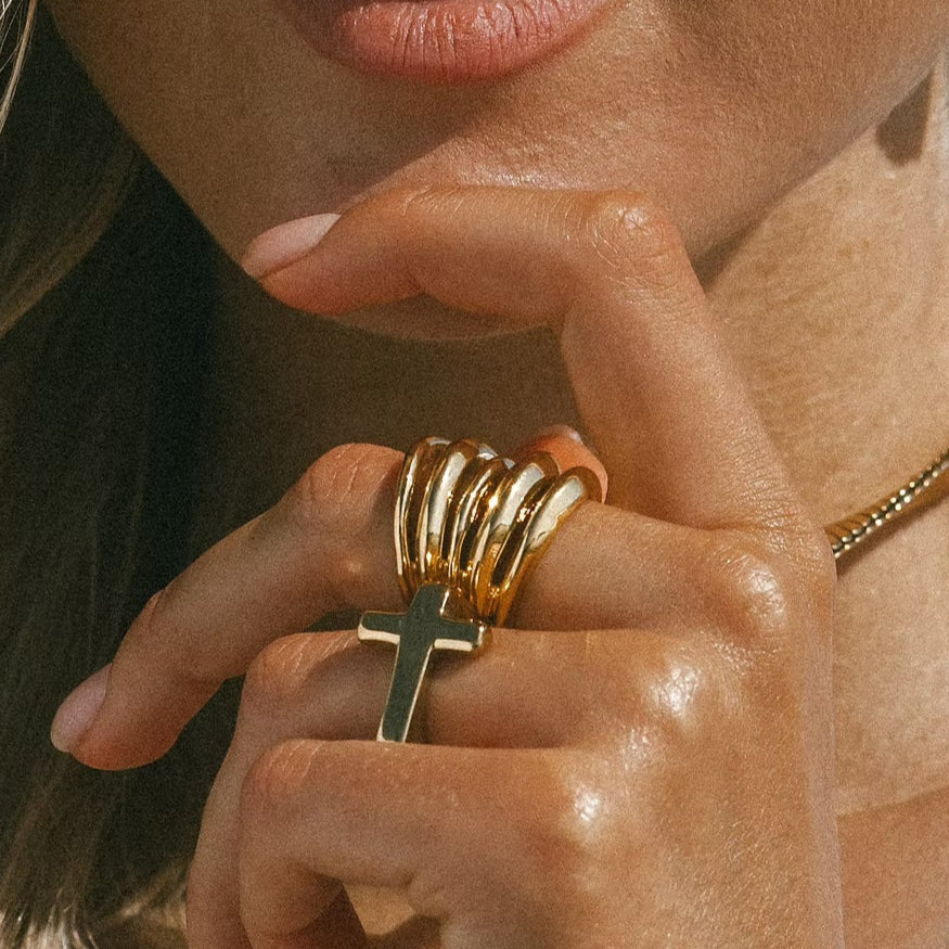 Blair Ring featuring stacked gold bands with black cross pendant, worn on hand with natural nails and beaded bracelet