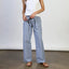 Woman wearing white sleeveless tank top and blue pinstriped linen pants with brown sandals, standing against white wall