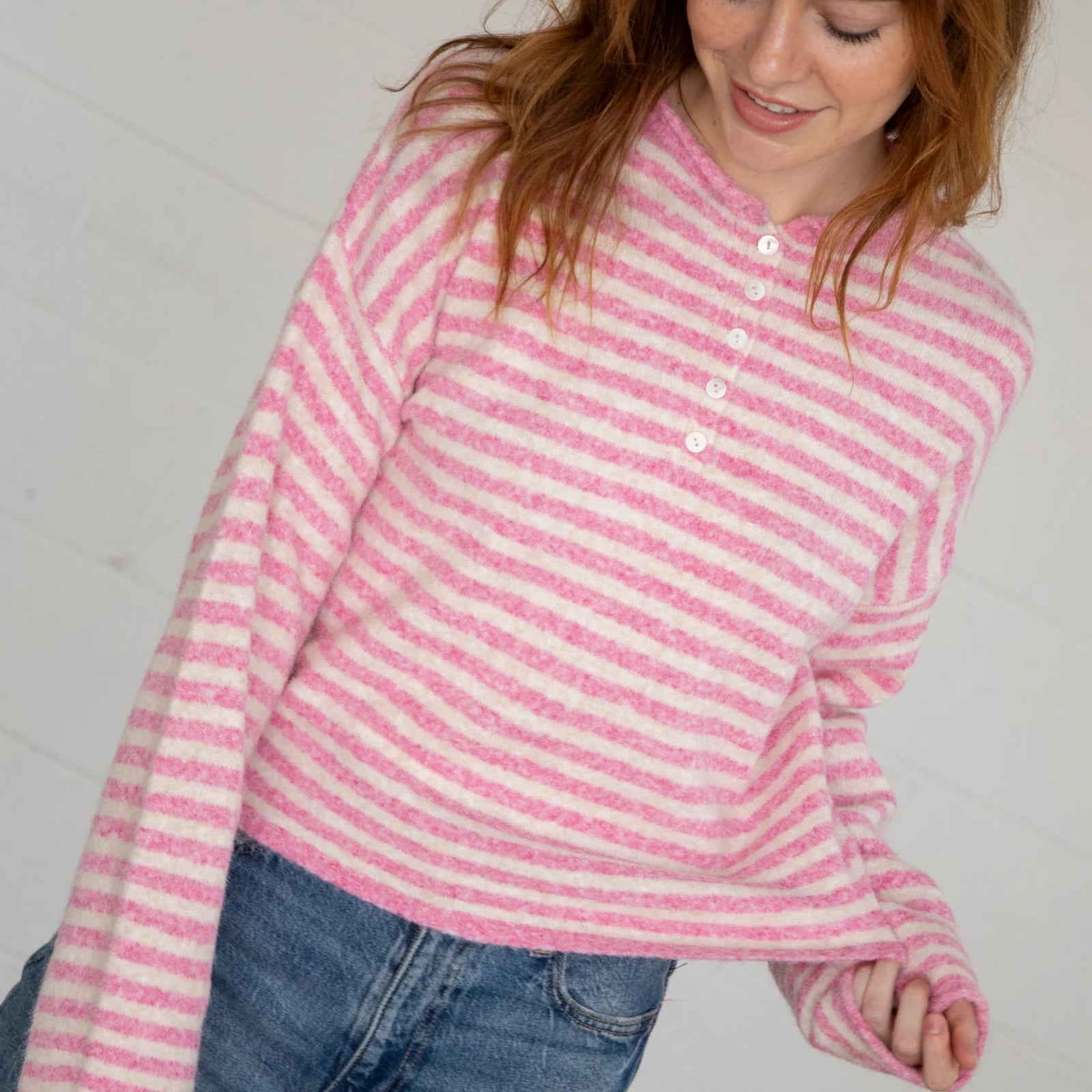 Woman wearing pink and cream striped henley with white button placket and long sleeves, paired with blue jeans