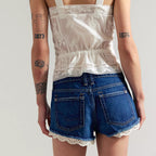 Person wearing a white lace top and blue shorts with a plain background