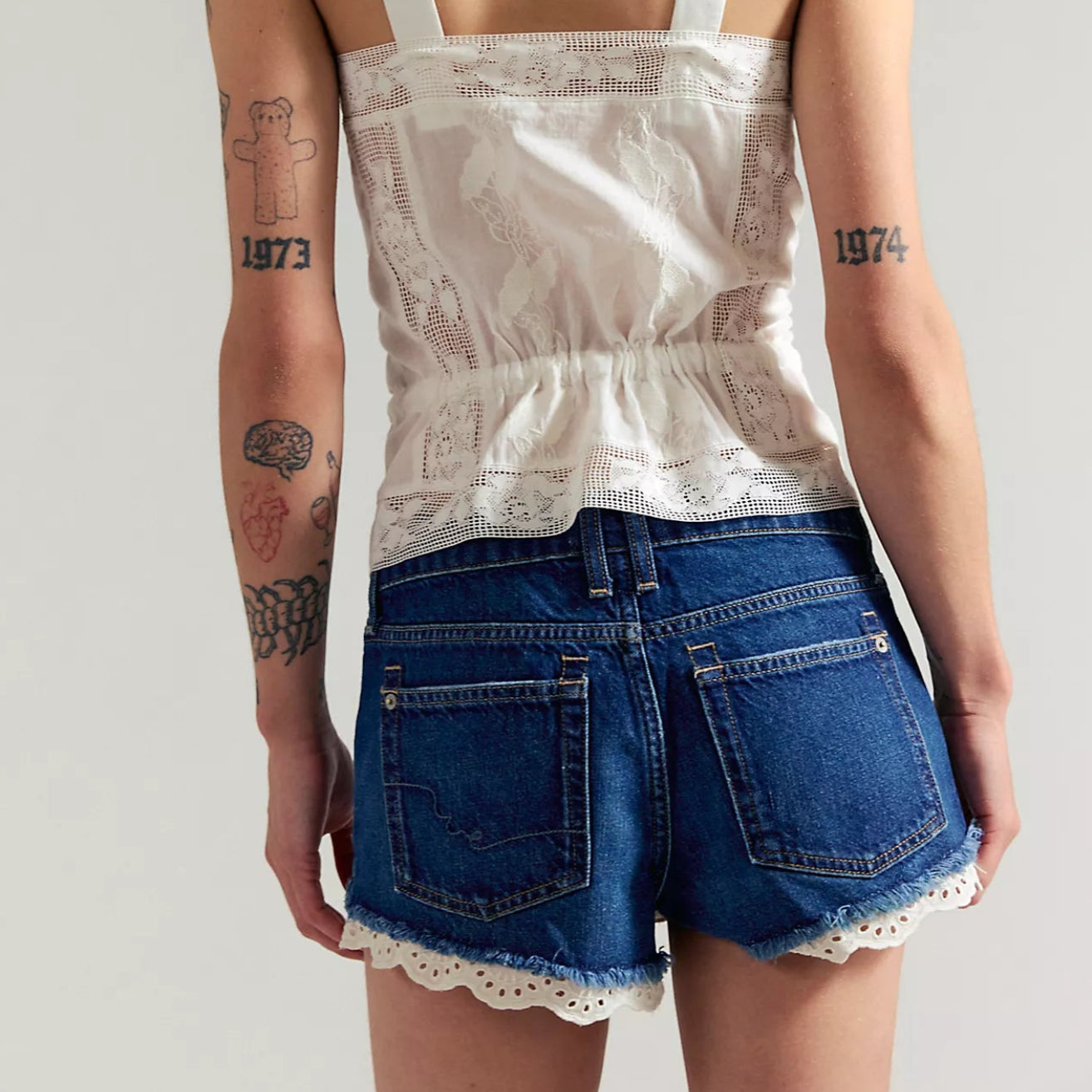 Person wearing a white lace top and blue shorts with a plain background