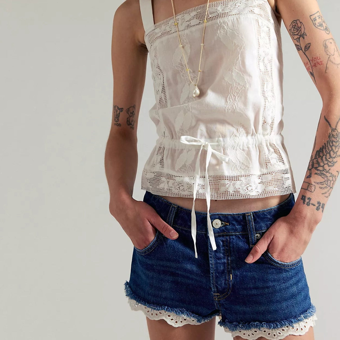 Person wearing a white lace top and denim shorts against a plain background