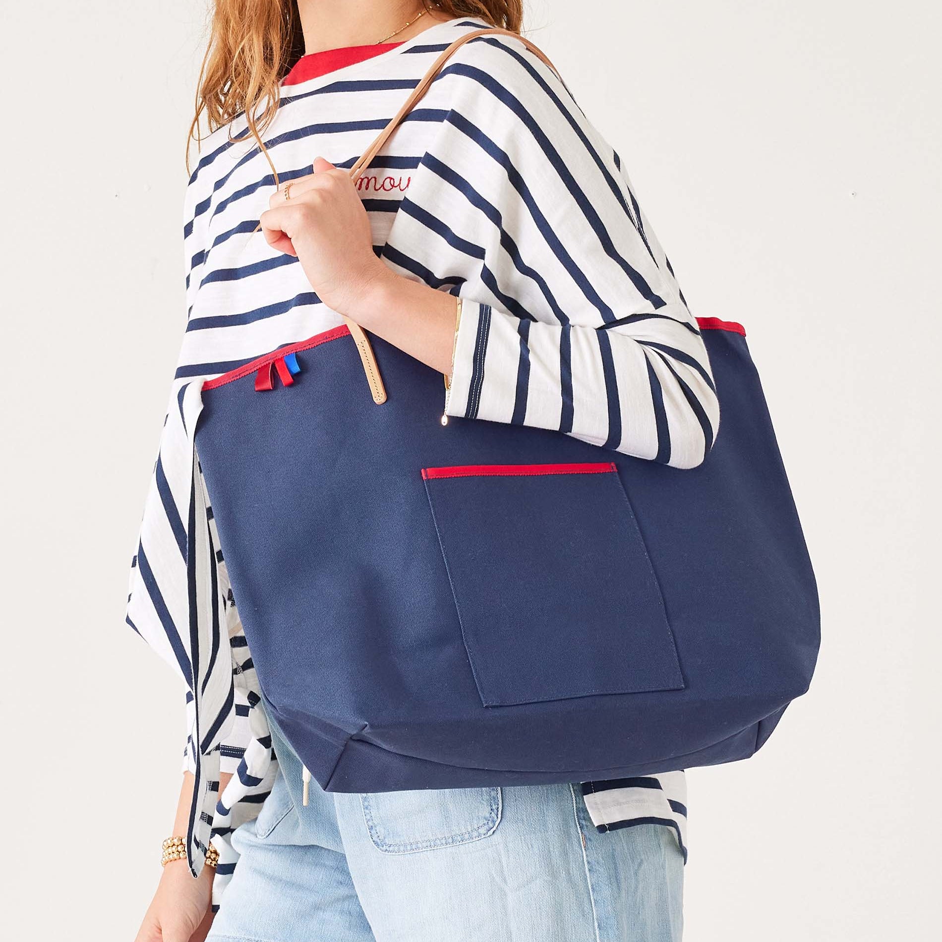 Woman wearing navy striped shirt carrying large navy canvas tote bag with red trim and tan handles