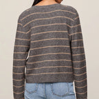 A woman shown from the back wearing a long-sleeve knit sweater with thin horizontal brown stripes on a heather gray base, paired with light blue jeans against a plain beige studio background.
