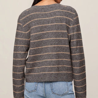 A woman shown from the back wearing a long-sleeve knit sweater with thin horizontal brown stripes on a heather gray base, paired with light blue jeans against a plain beige studio background.