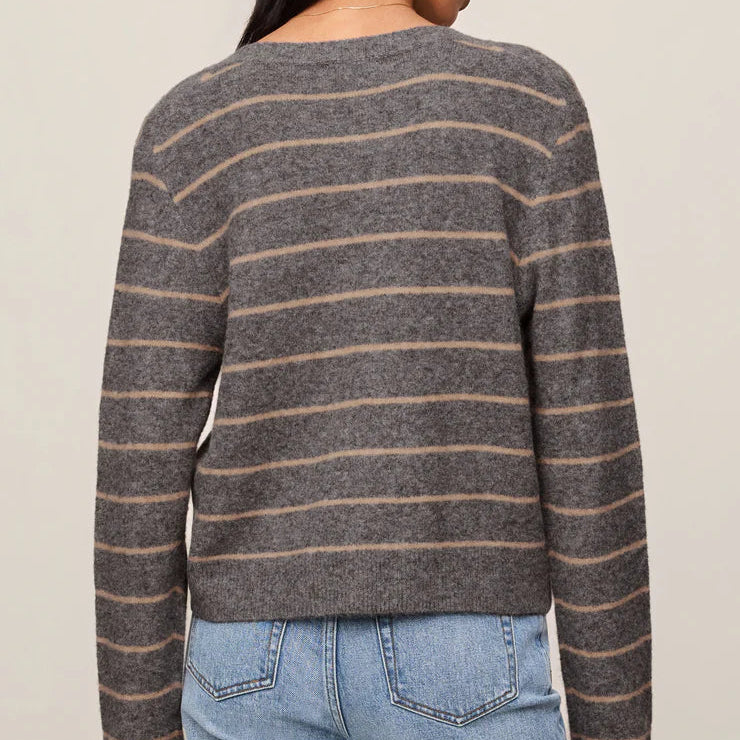 A woman shown from the back wearing a long-sleeve knit sweater with thin horizontal brown stripes on a heather gray base, paired with light blue jeans against a plain beige studio background.