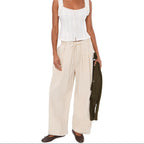 Woman wearing cream pull-on pants with drawstring waist and white textured tank top, holding olive cardigan