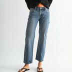 A model wearing a black ribbed button-front mock neck cardigan, blue cropped flare jeans, and black flip-flops, standing against a light gray studio background.