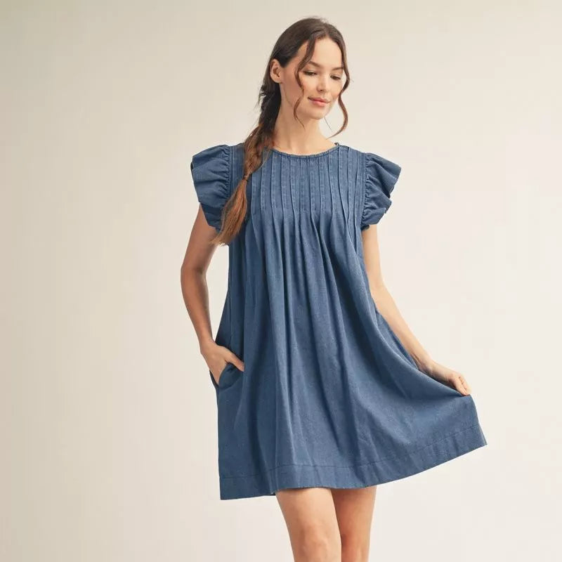Woman wearing blue pleated mini dress with puffed short sleeves and front pockets, standing against neutral background