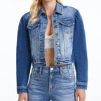 Woman wearing cropped blue denim jacket with puff sleeves and button front over white crop top and light denim jeans