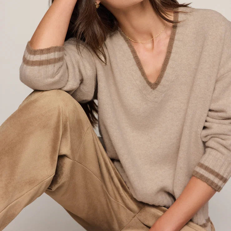 A woman wearing a beige v-neck knit sweater with striped cuffs and matching beige pants, posed against a light neutral studio background. Main image