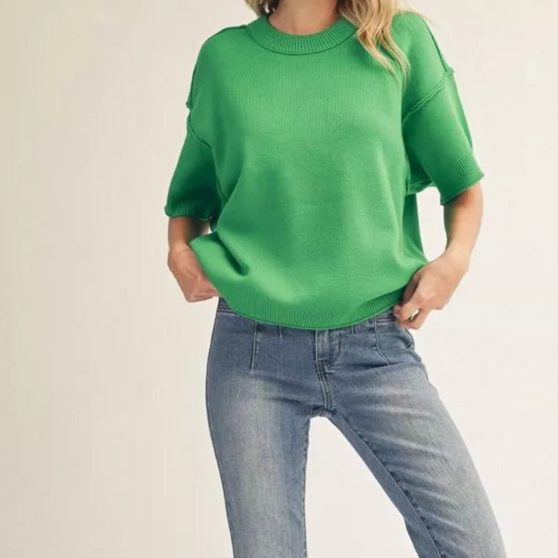 Woman wearing a green sweater and blue jeans on a plain background