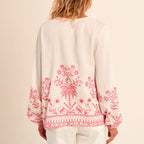 Person wearing a light-colored blouse with pink floral embroidery on a plain background