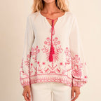 Woman wearing a white blouse with pink embroidery and tassel on a beige background