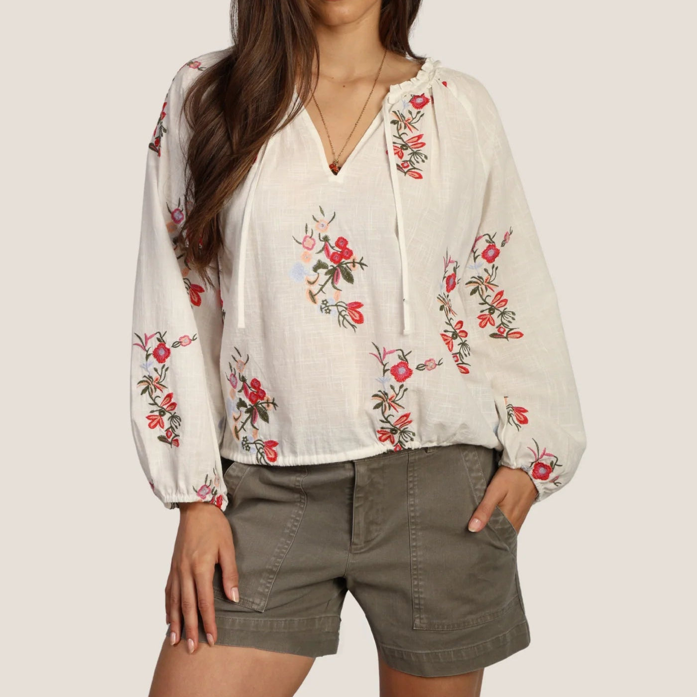 Woman wearing a white blouse with floral embroidery and green shorts on a plain background