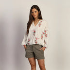 Woman wearing a floral blouse and shorts against a plain background