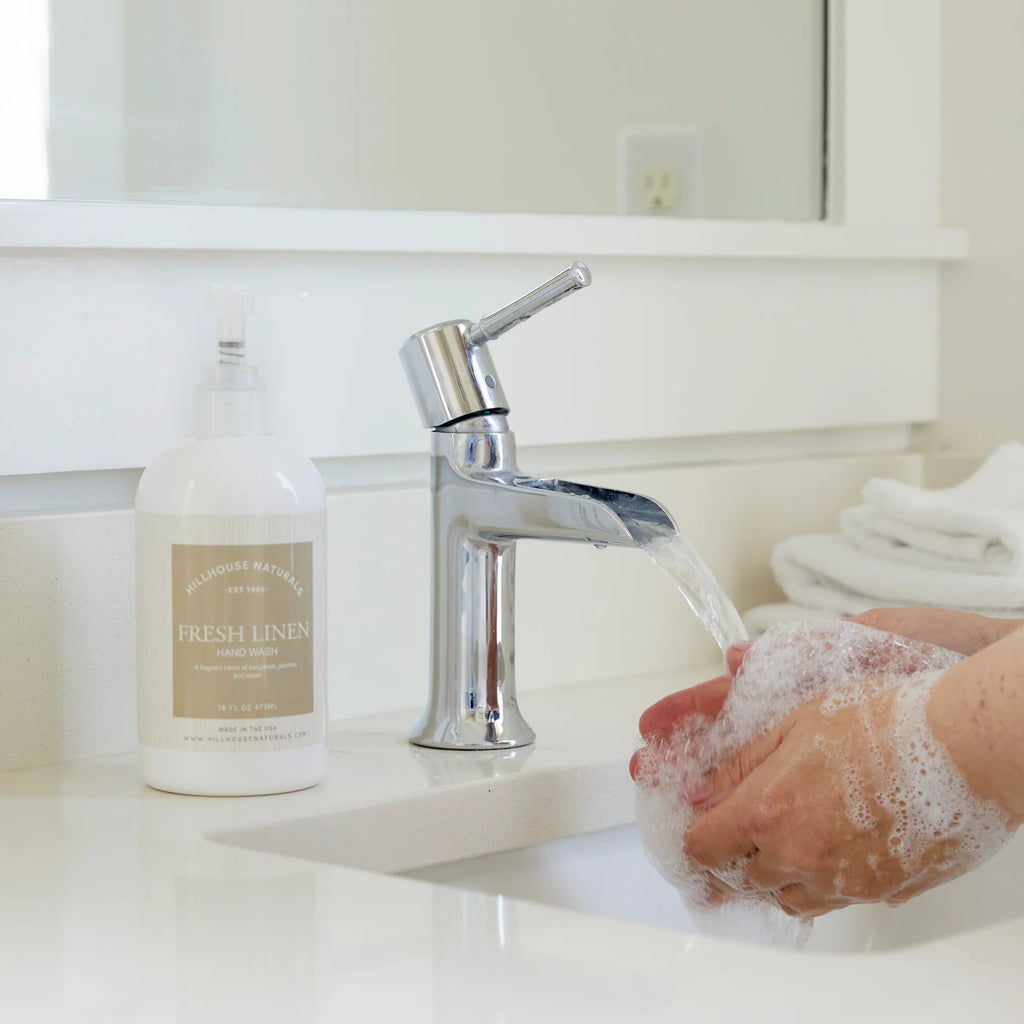 Hands lathered with Fresh Linen hand wash under running water at bathroom sink with chrome faucet